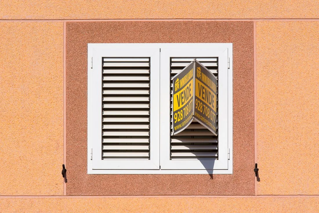 Cartel de «Se vende» de una inmobiliaria colgado en la persiana de una ventana
