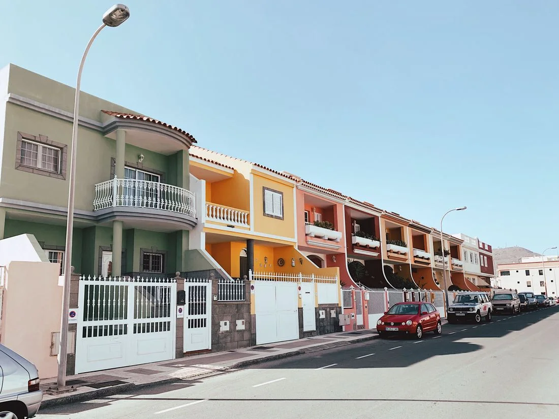 Calle de adosados españoles de colores, con coches aparcados y farolas