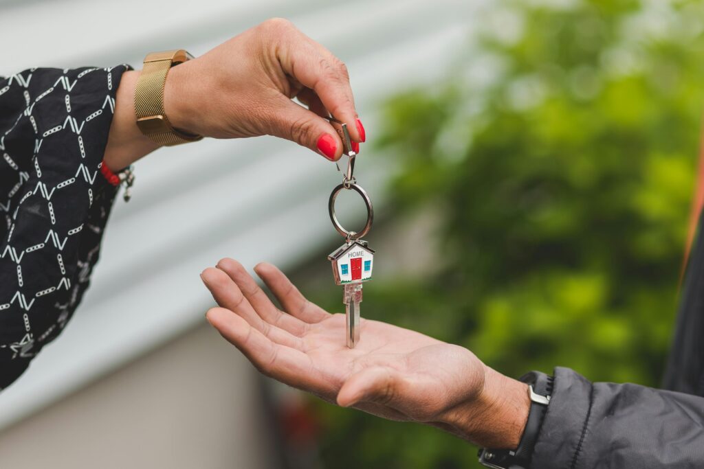 pexels-photo-8292791-8292791 Close-up of a hand handing over a key with a house keychain, symbolizing real estate transaction.